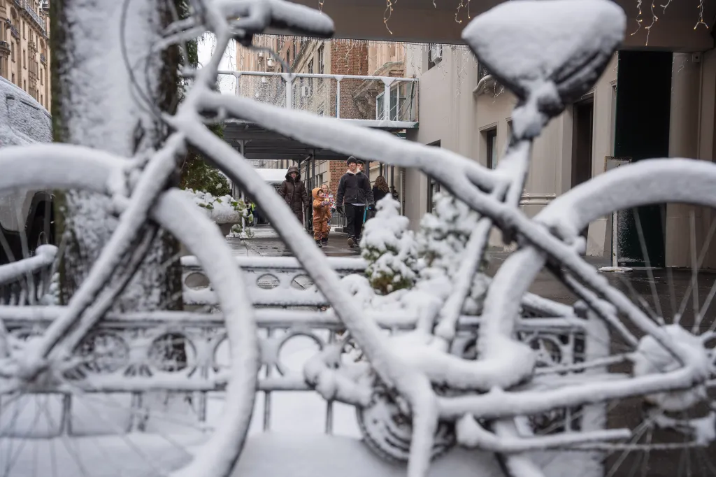 Snow-covered bicycle in the foreground with people walking down a street in Manhattan.