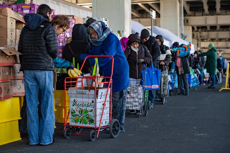Workers and volunteers hand out food to people in line at La Colaborativa's food pantry in Chelsea, Massachusetts