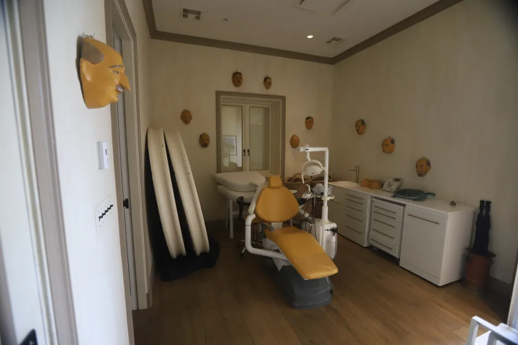 A room with a dental chair, white cabinets, and multiple decorative head masks on the walls.