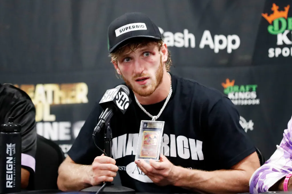 Logan Paul at a press conference holding up a Charizard Pokemon card in a graded slab.