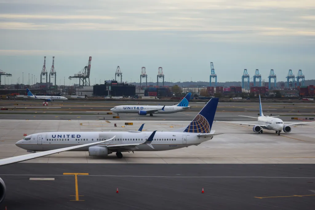 Multiple United airplanes on the runway with port cranes in the background.