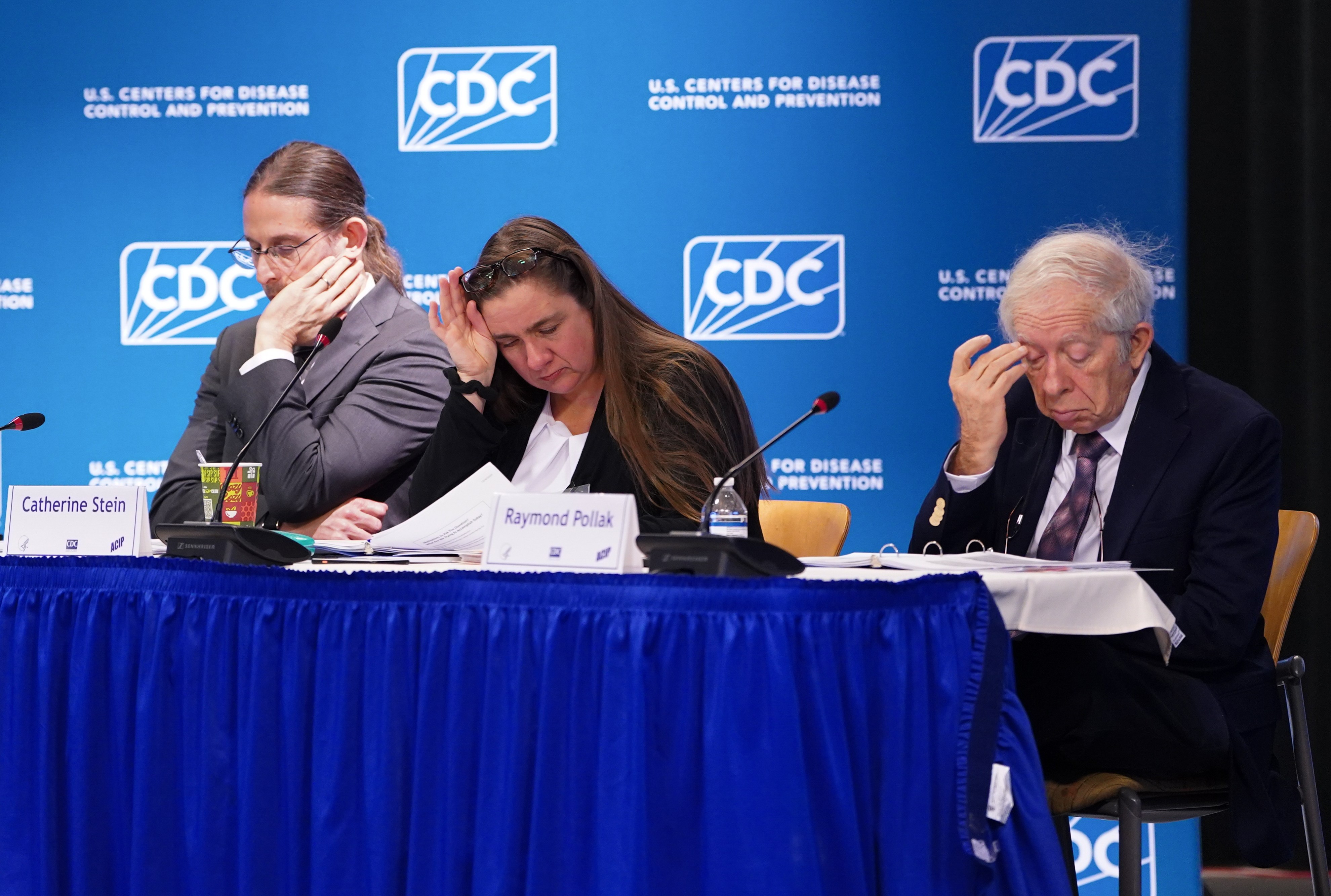 Three people sit in front of a blue CDC banner looking visibly upset.