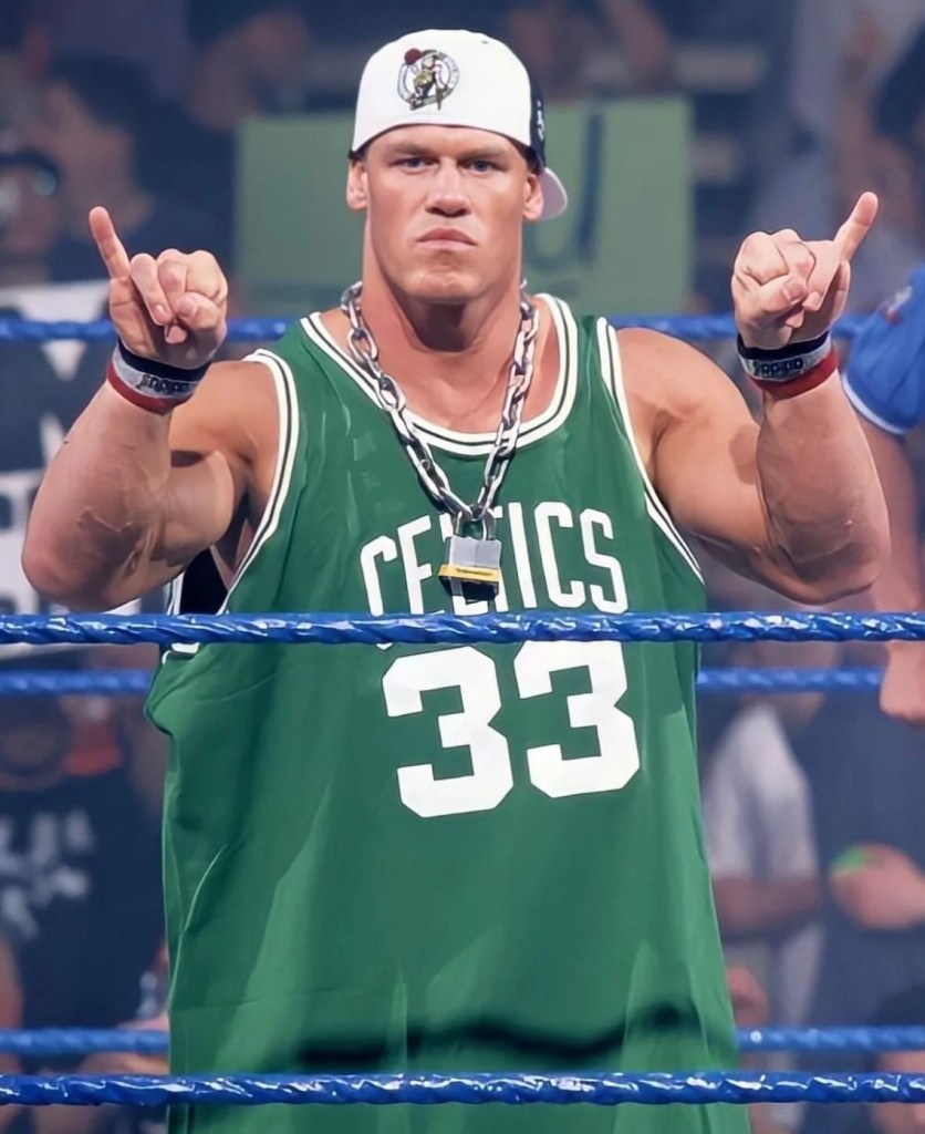 John Cena wears a Boston Celtics jersey with his signature padlock and backwards cap.