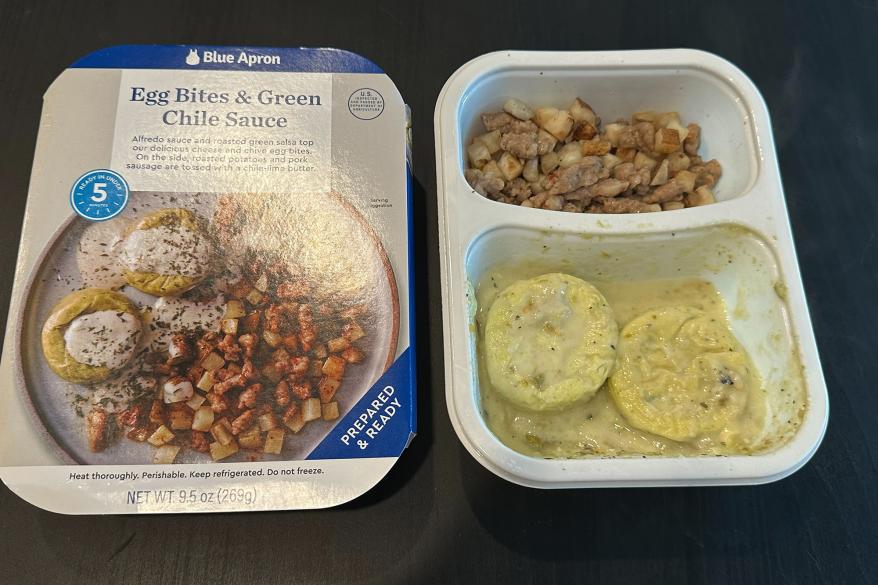 A pre-made breakfast in a container on a table, featuring fluffy eggs and spicy sauce