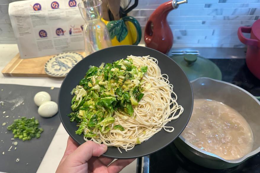 A person holding a plate of noodles and vegetables