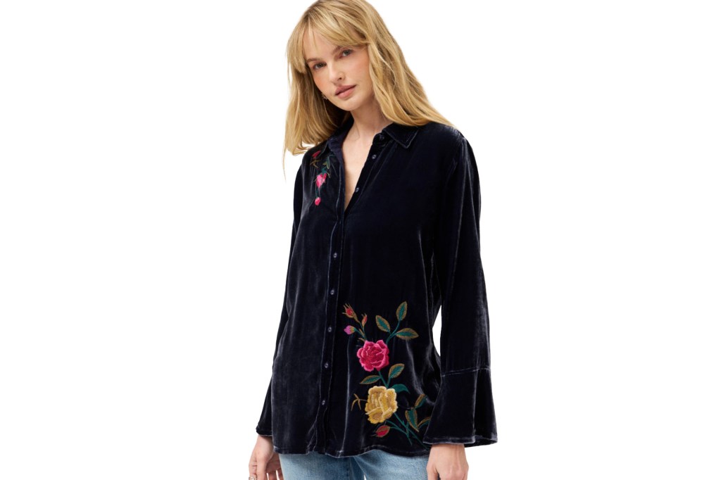 A woman wearing a dark blue velvet button-up shirt with floral embroidery.