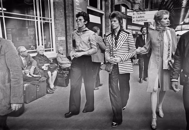 English singer, songwriter and actor David Bowie at King's Cross Station in London with his wife Angie Bowie (right) and English fashion designer Antony Price (on left), as he leaves for Aberdeen in Scotland on his Ziggy Stardust tour, UK, 15th May 1973.