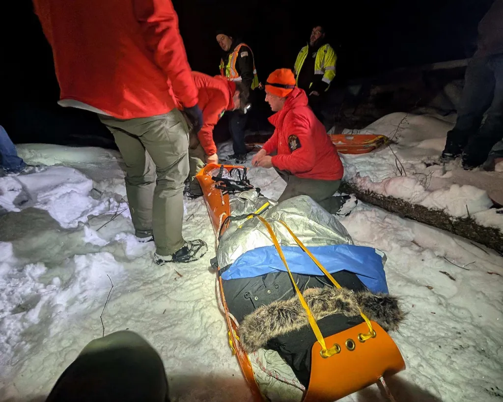 Firefighters and emergency personnel attending to a patient in a rescue sled in the snow at night.