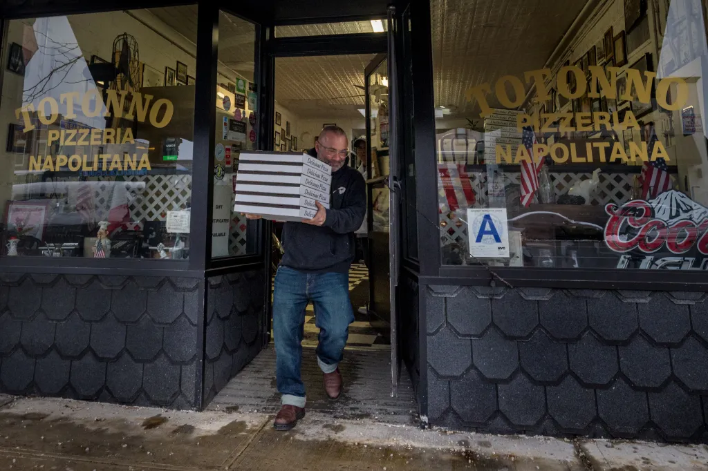 Man carrying multiple pizza boxes out of Totonno's Pizzeria Napolitana.