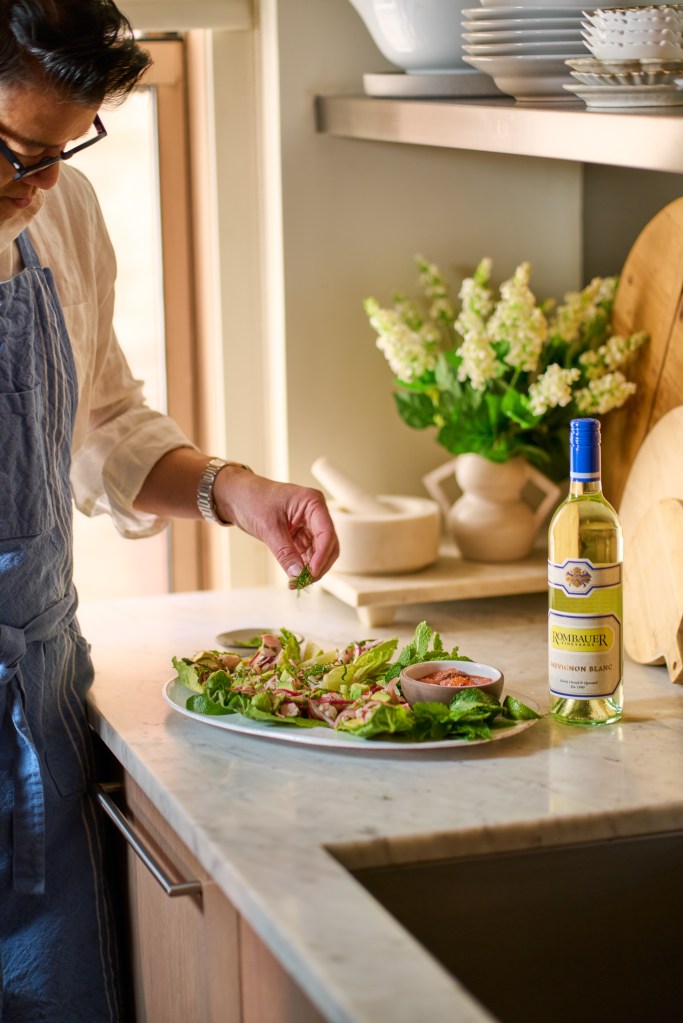A person garnishing mahi-mahi larb with herbs on a kitchen counter with a bottle of Rombauer Vineyards Sauvignon Blanc.