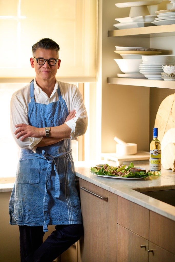 Peter Som standing in a kitchen with Mahi Mahi Larb and a bottle of Rombauer Vineyards Sauvignon Blanc.