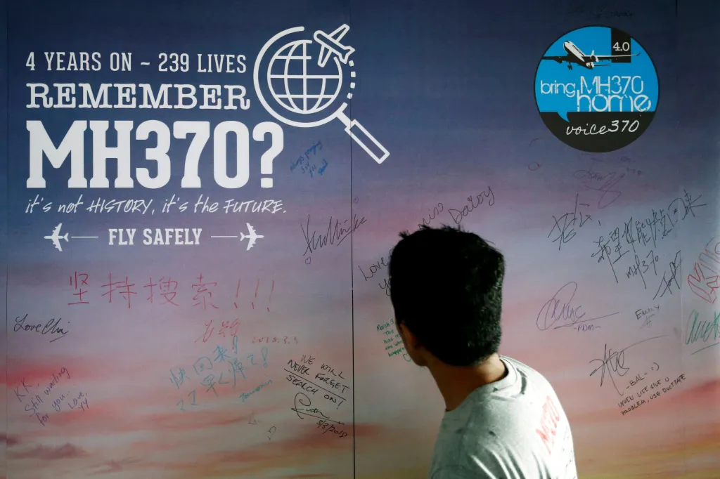 A man looking at a message board for passengers onboard missing MH370 in Kuala Lumpur, covered in messages and signatures from the public.