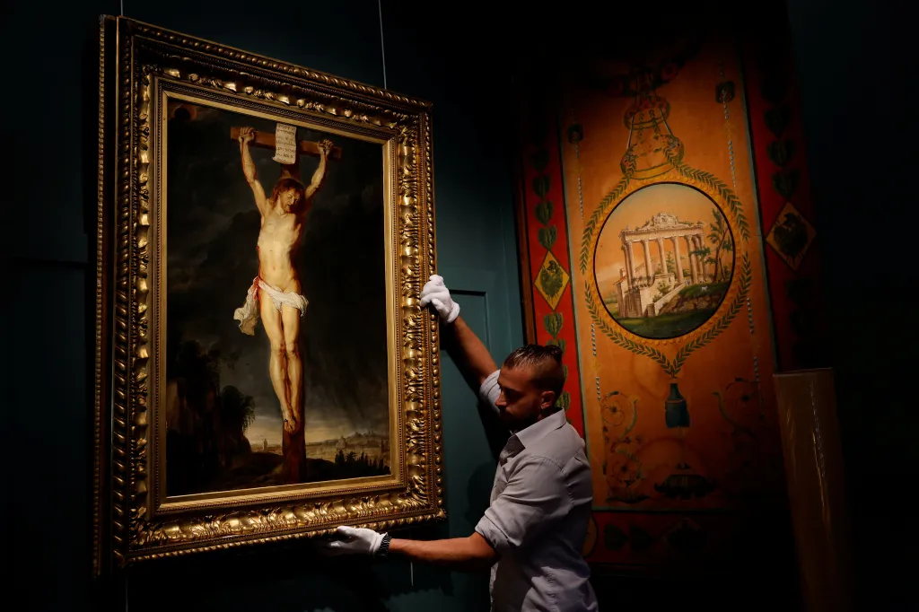 A man in white gloves carefully adjusts a Rubens masterpiece, a framed painting of Christ on the cross.