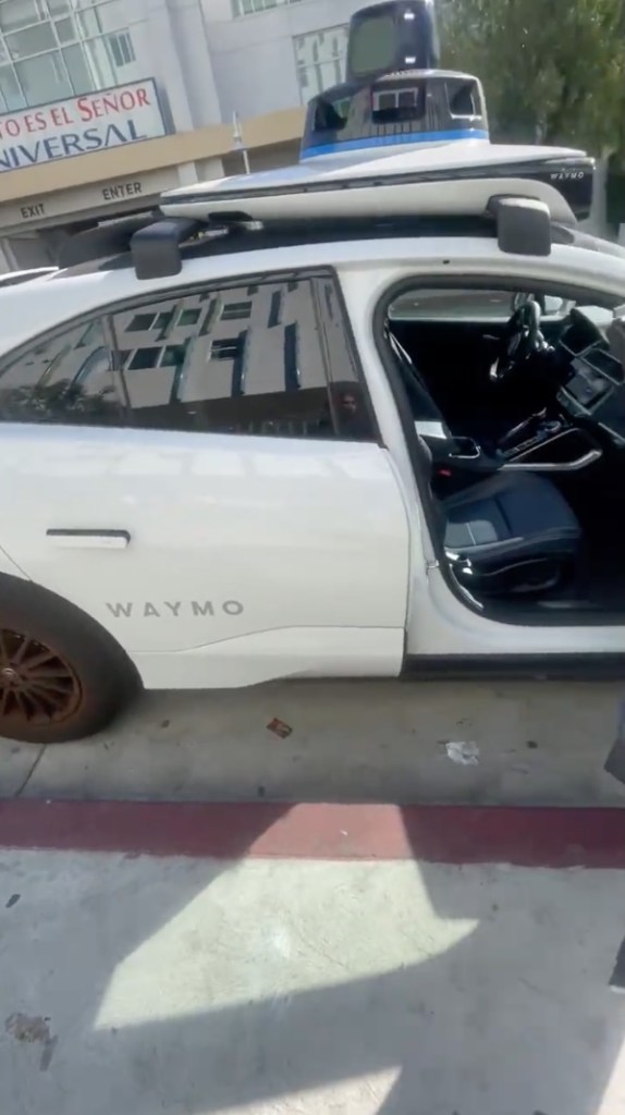 White Waymo autonomous vehicle parked on the side of a street.