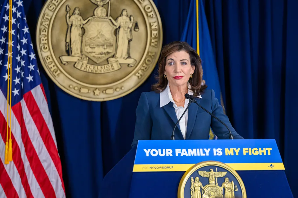 Governor Kathy Hochul at a podium with the New York State seal and an American flag in the background.