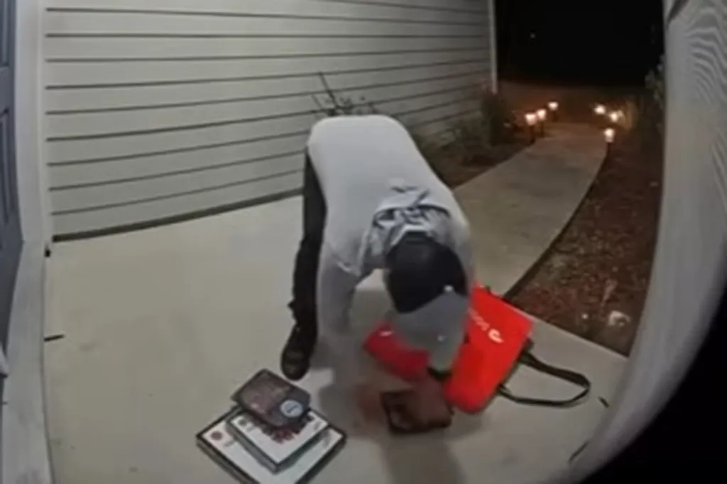 A DoorDash delivery driver bending over to pick up food that fell out of a red delivery bag.
