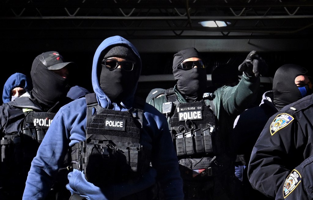 Several law enforcement officers, some in balaclavas, wearing vests with