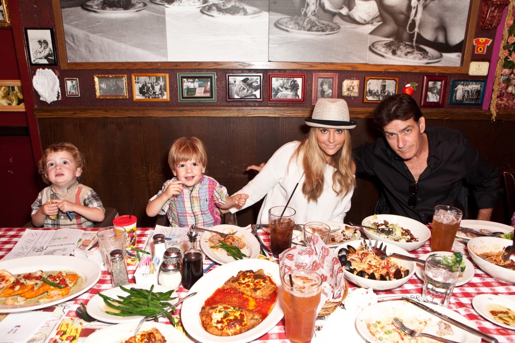 Charlie Sheen, Brooke Mueller, and their two young sons, Max and Bob, at a restaurant table with plates of food and drinks.