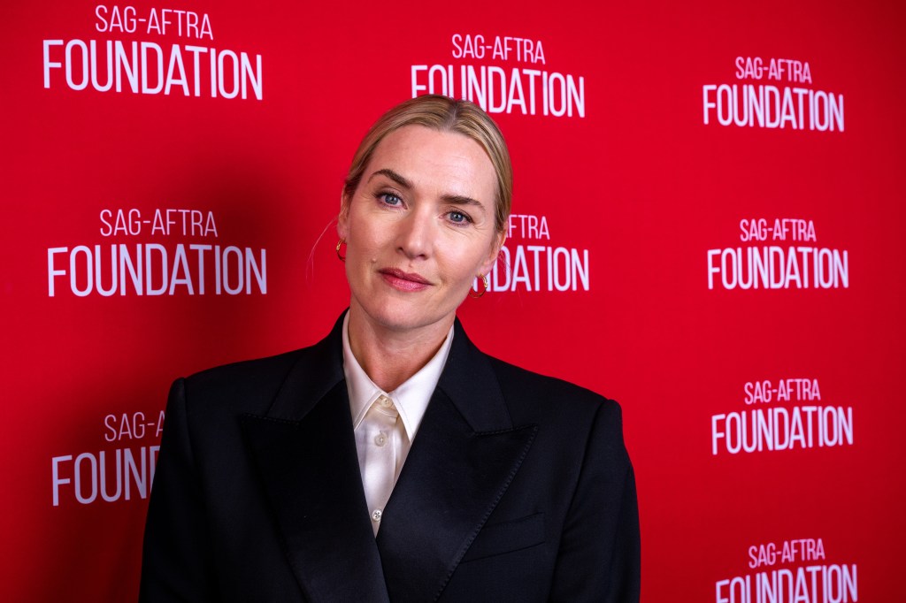 Actress Kate Winslet poses in front of a red backdrop with the white