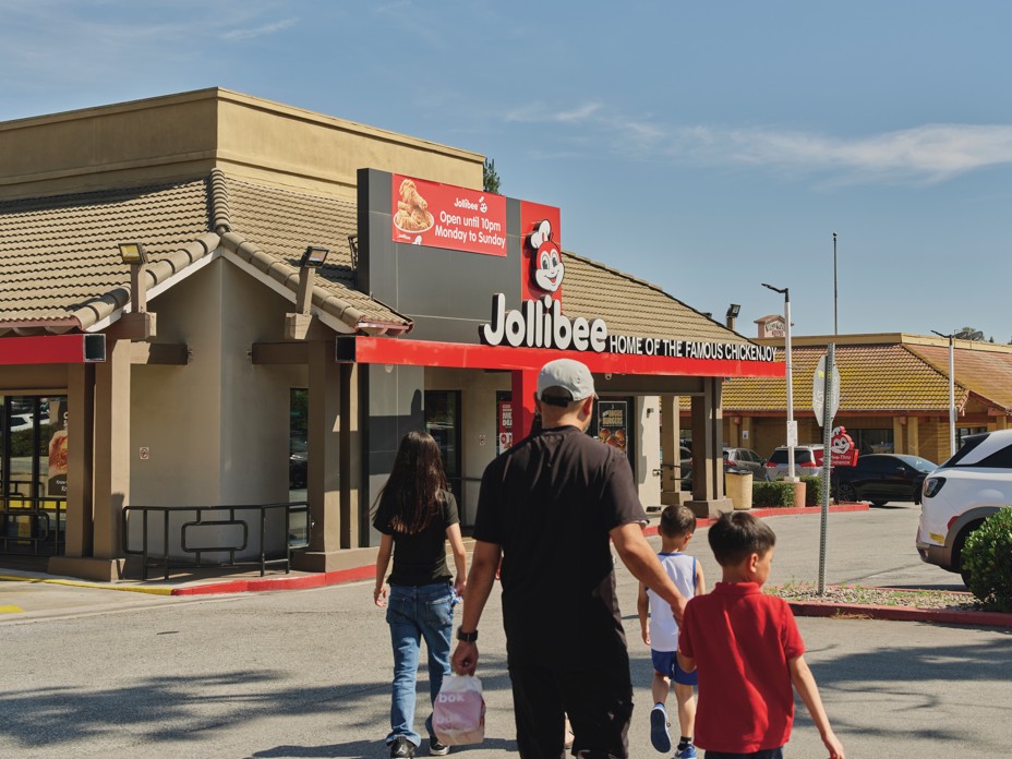 photo from behind of family with children walking through parking lot toward a Jollibee restaurant
