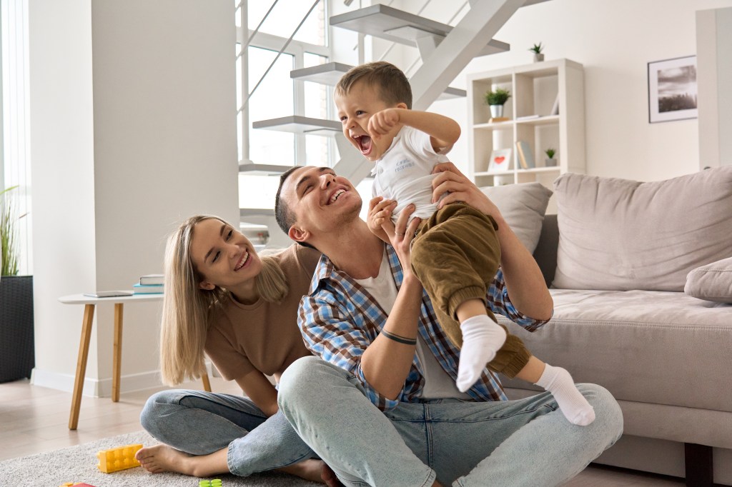 Parents playing with their son, who is laughing while being held by his father.
