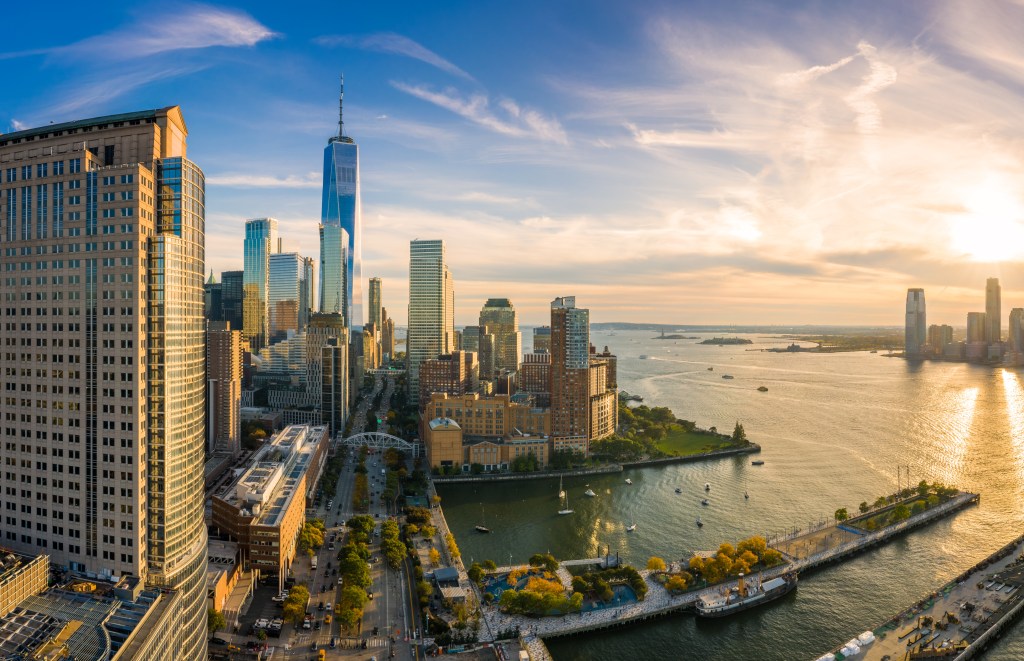 Aerial view of the Lower Manhattan skyline at sunset with the Hudson River reflecting the golden light.