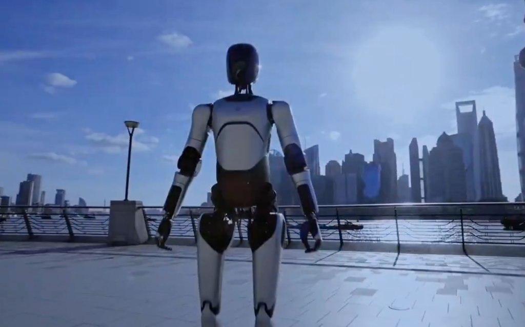 AgiBot A2 humanoid robot walking outdoors along a waterfront with a city skyline in the background.