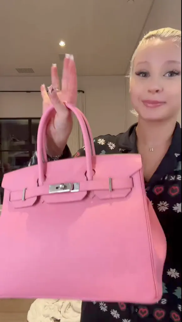 Alabama Barker holds up a pink Birkin bag.
