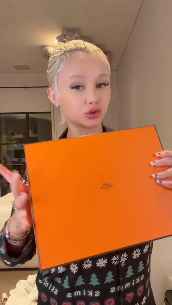 Alabama Barker showing off a large orange Hermès box.