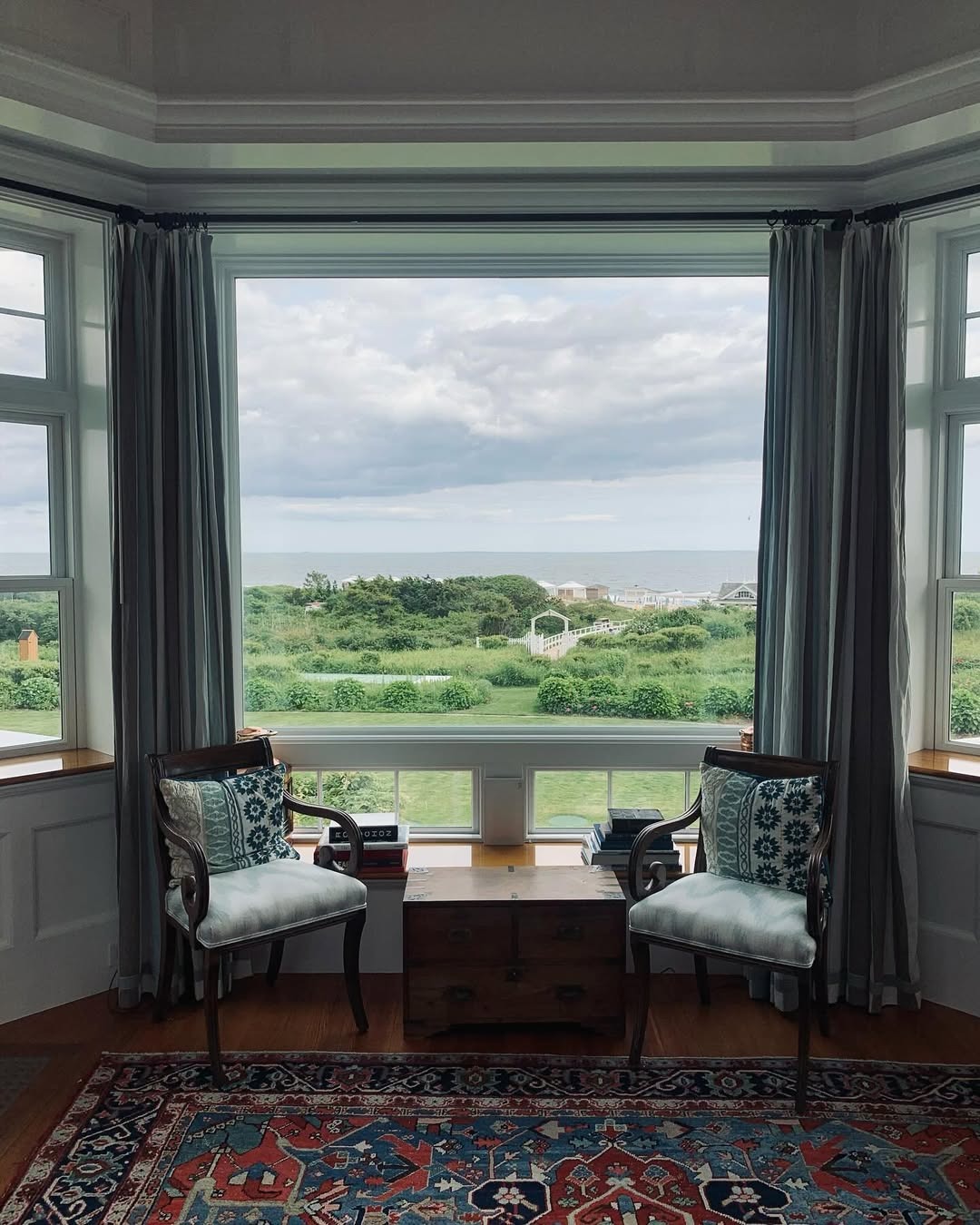A sitting area with chairs and a small table looking out a window to a green landscape and the ocean.