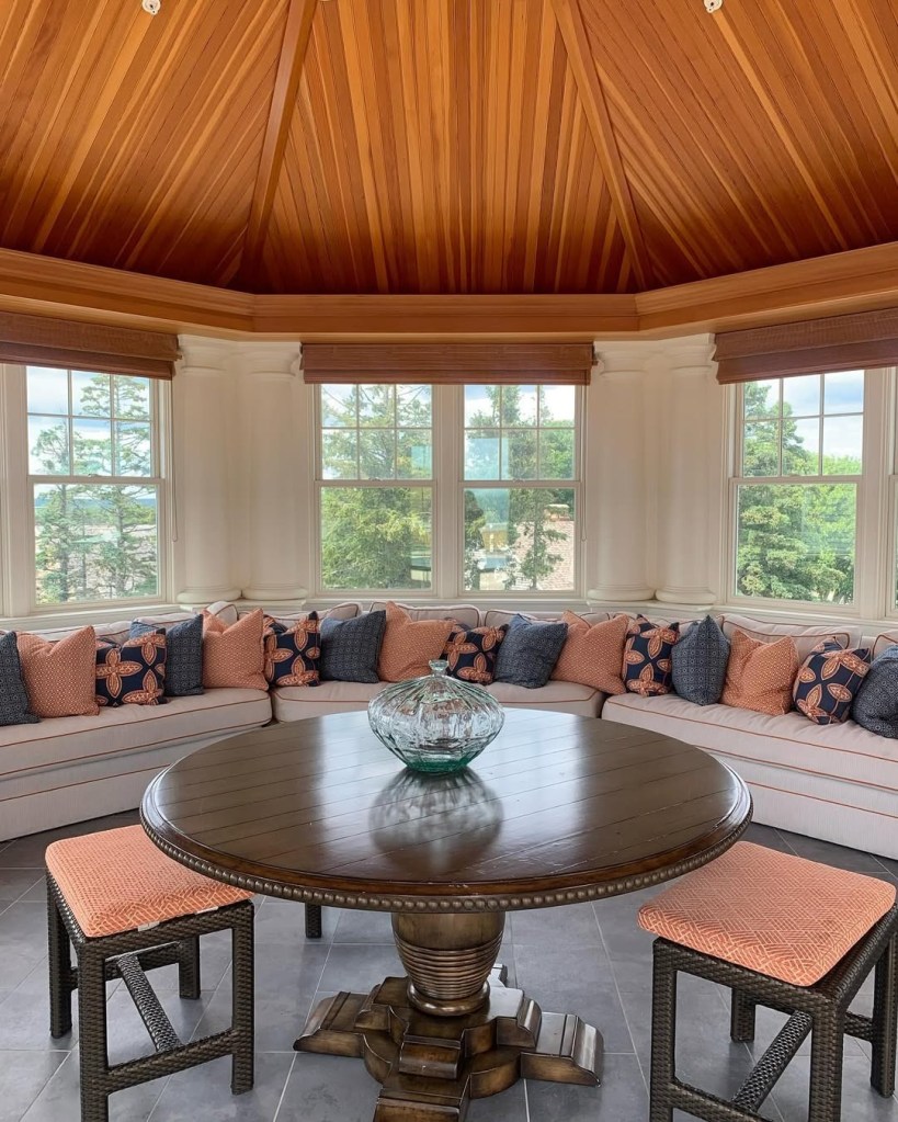 A sunroom at Ocean House in Rhode Island with a wooden table, built-in sofa with coral and blue pillows, and large windows.