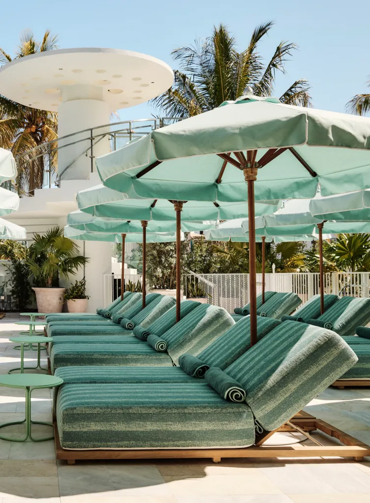 Long-shot of lounge chairs with green and white striped cushions underneath matching umbrellas on a patio.