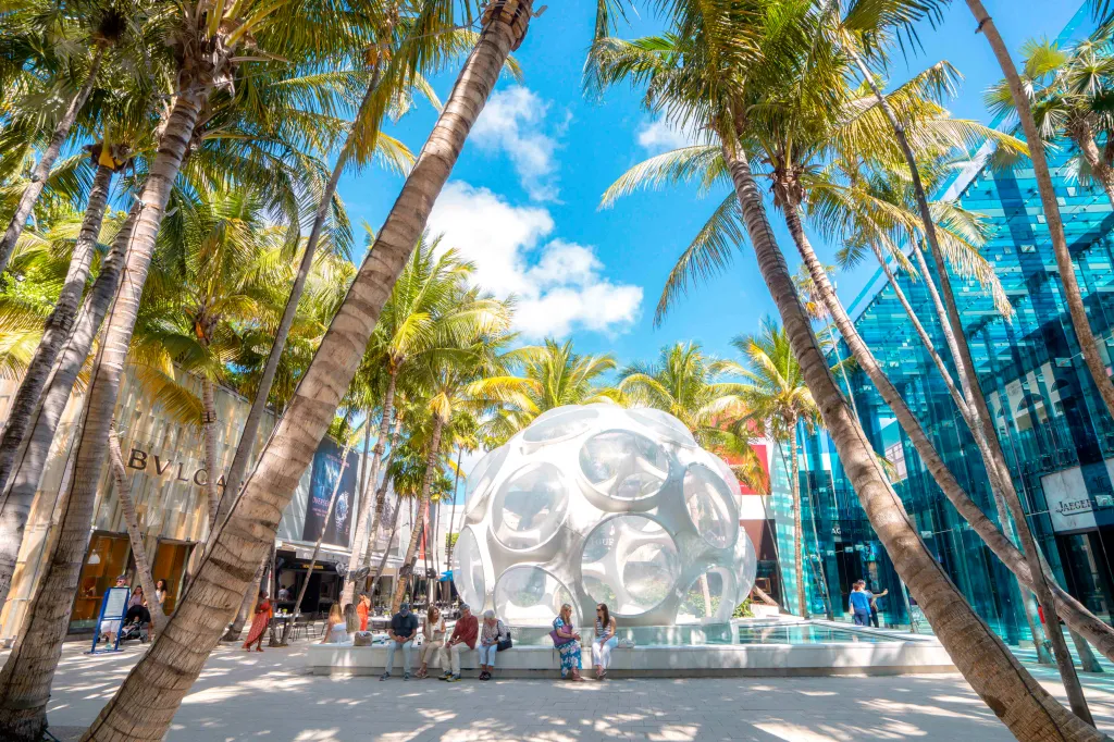 The Miami Design District features palm trees, luxury storefronts, and a large spherical sculpture.