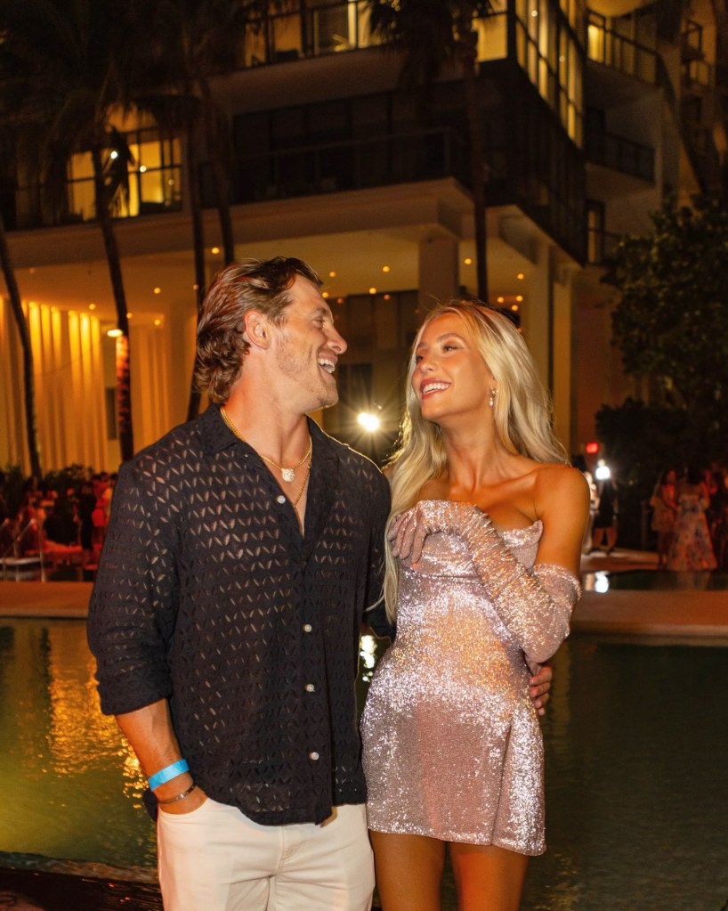 Alix Earle and Braxton Berrios smiling at each other by a pool at night.
