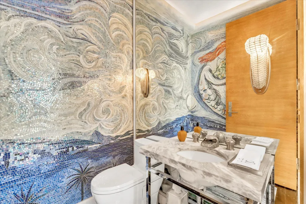 Bathroom with mosaic tiles depicting an ocean scene, a toilet, a marble vanity with a sink, and a light-wood door.