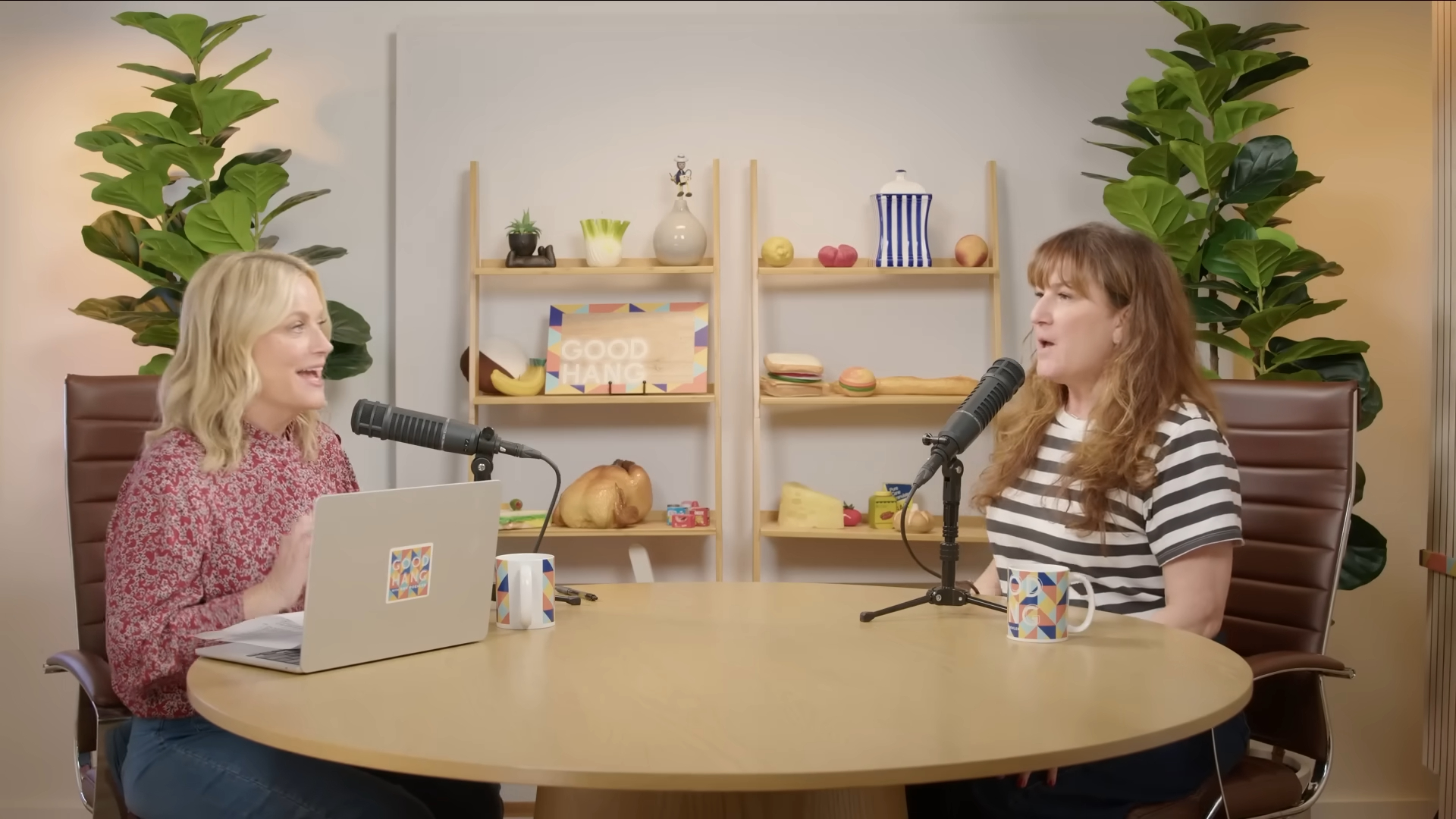 Amy Poehler and a woman in a striped shirt sitting at a round table with microphones.