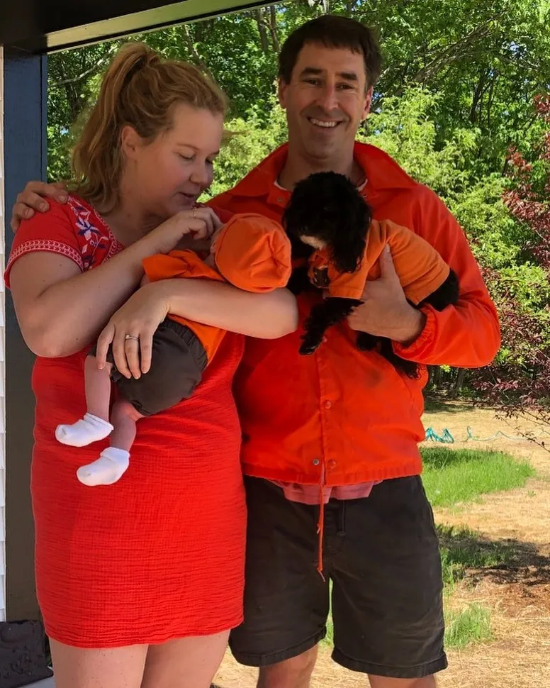 Amy Schumer, holding a baby, and Chris Fischer, holding a black dog, all wearing orange.