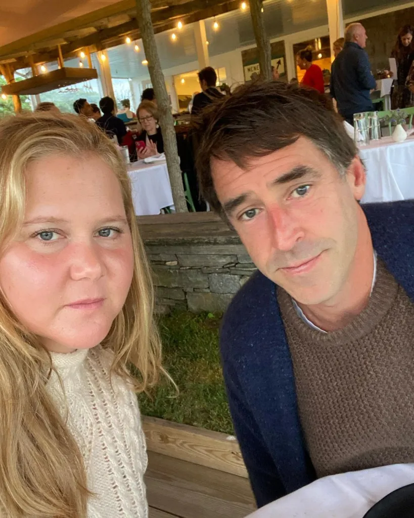Amy Schumer and a man sitting at a table with other people in the background.
