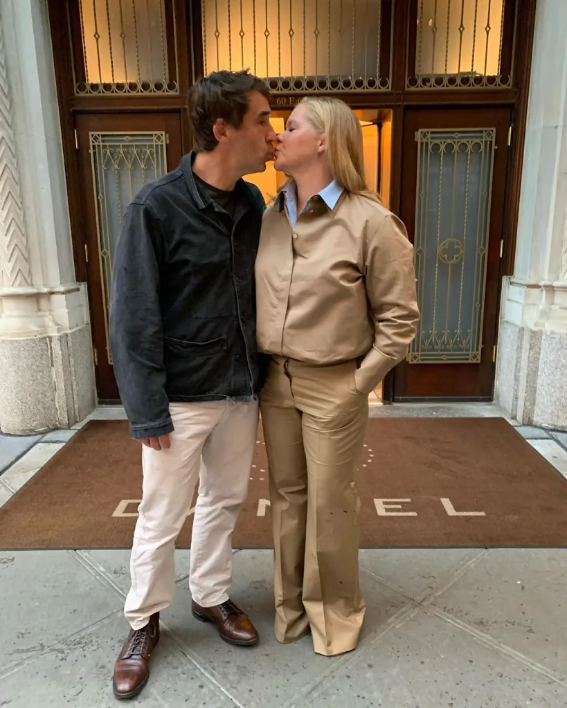 Amy Schumer and a man kiss outside a building.