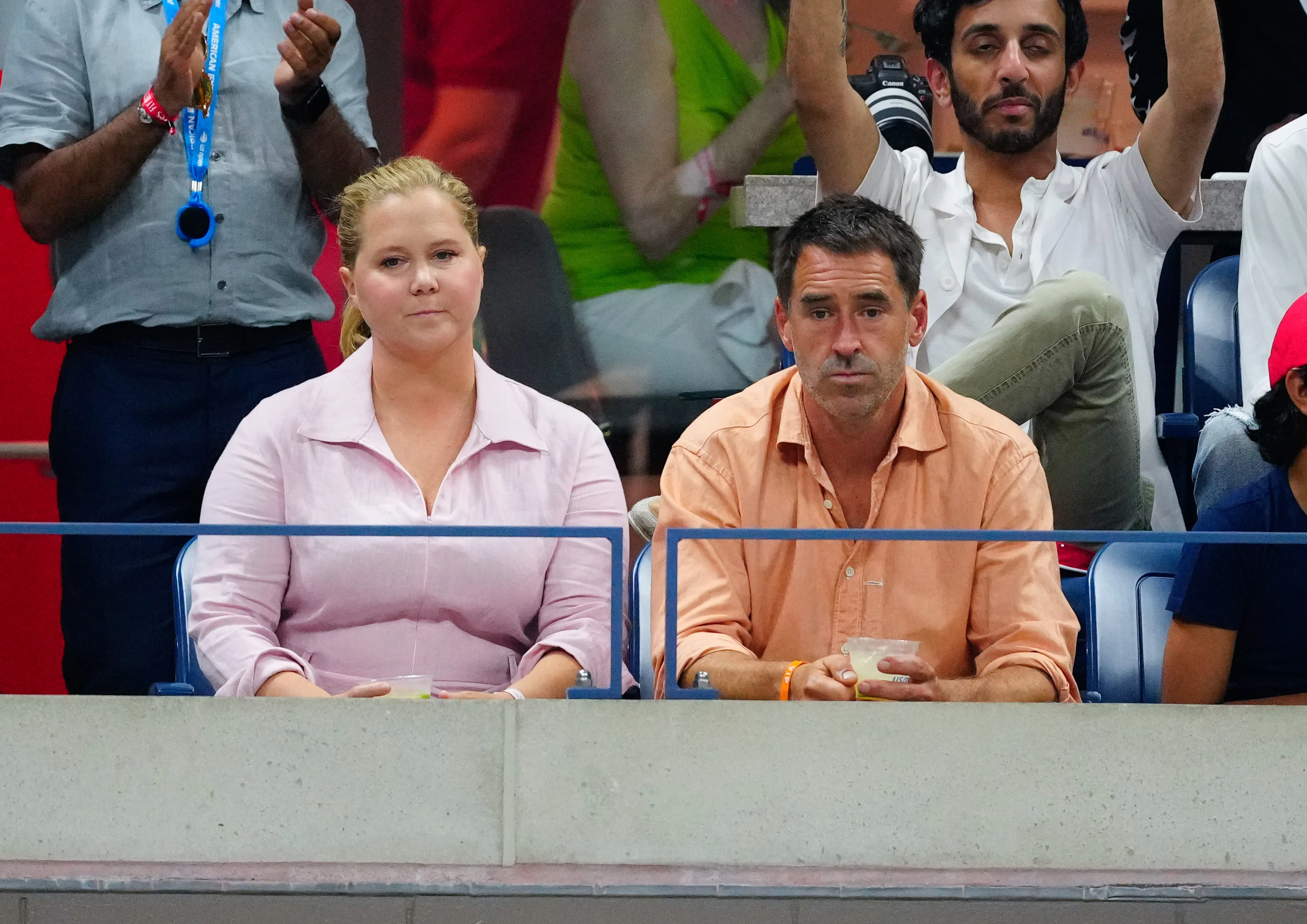 Amy Schumer in a light pink shirt and Chris Fischer in an orange shirt sitting at the US Open.