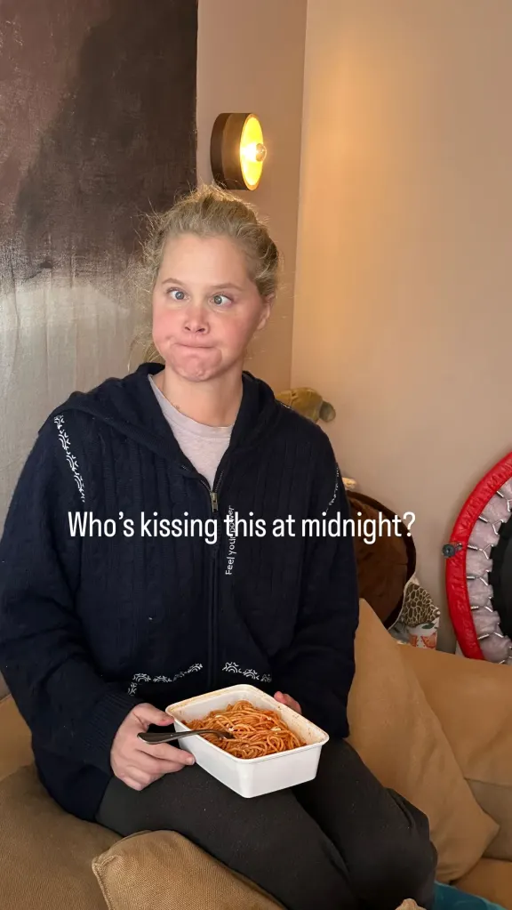 Amy Schumer makes a funny face while holding a container of spaghetti.