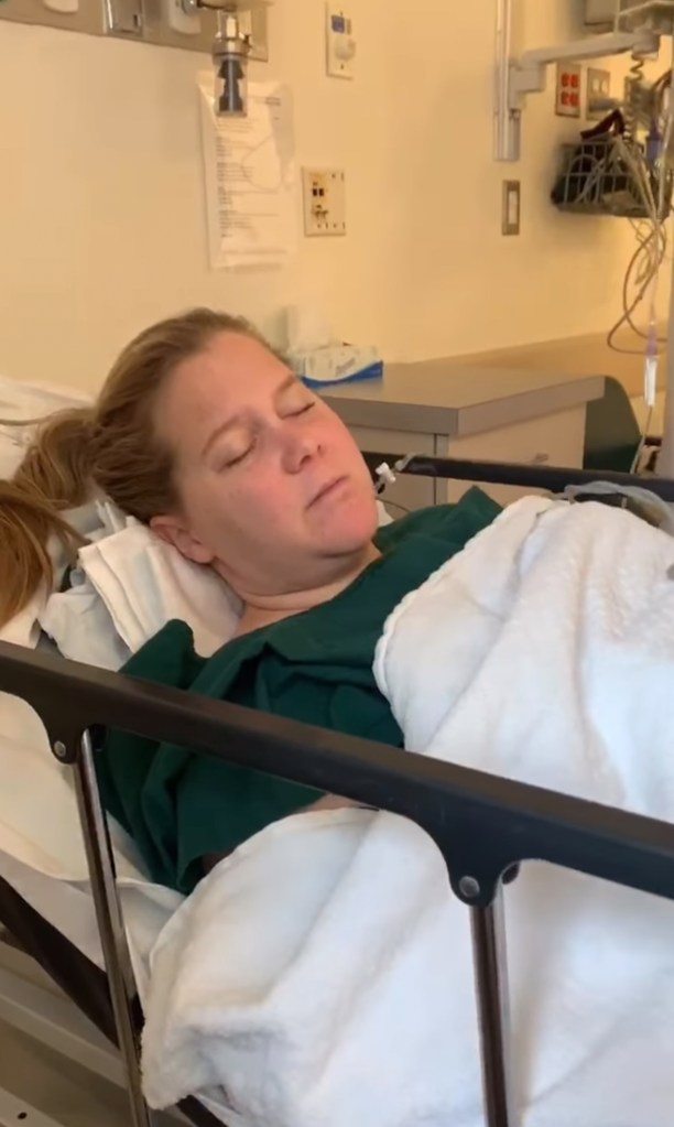 Amy Schumer in a hospital bed with her eyes closed.