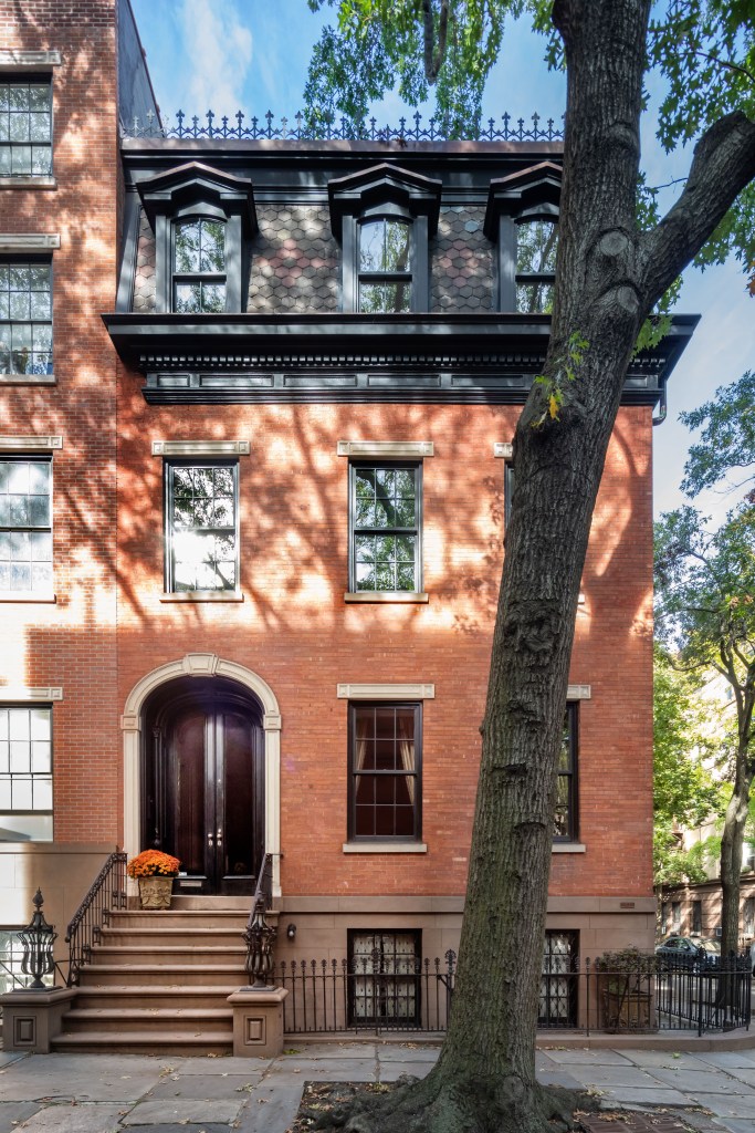 Historic brick townhouse with a dark arched double door entryway, black wrought-iron railings, and a dark shingled top floor.