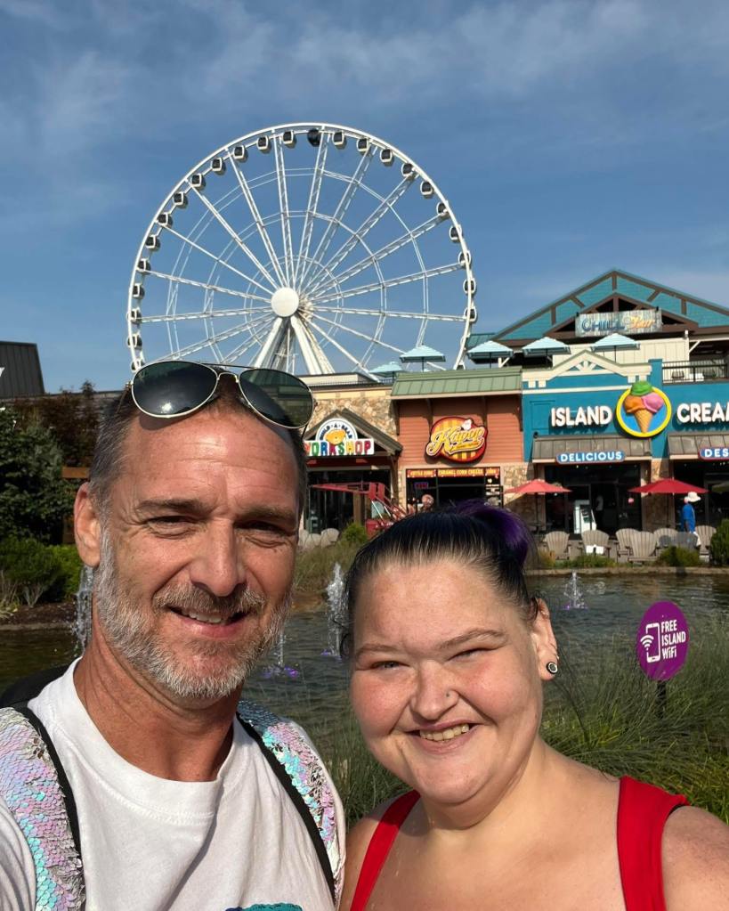 Amy Slaton and a man smiling with a ferris wheel and shops in the background.