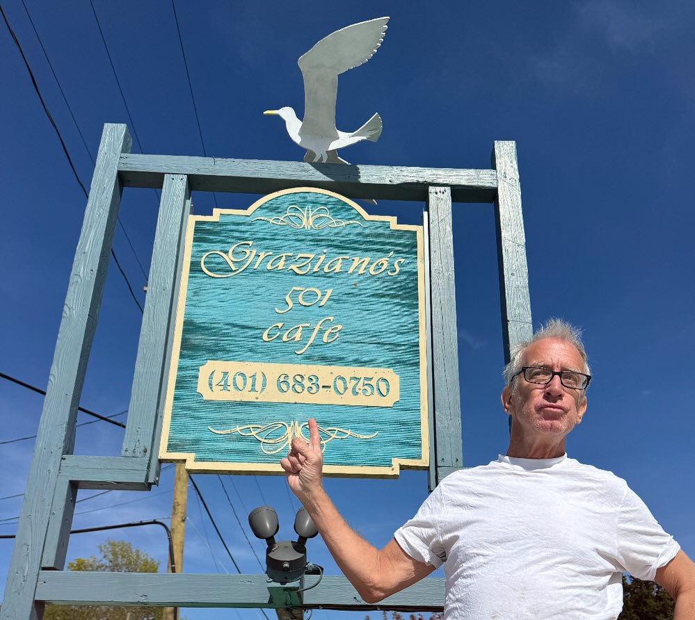 Andy Dick making a peace sign next to a sign for Graziano's 501 Cafe.