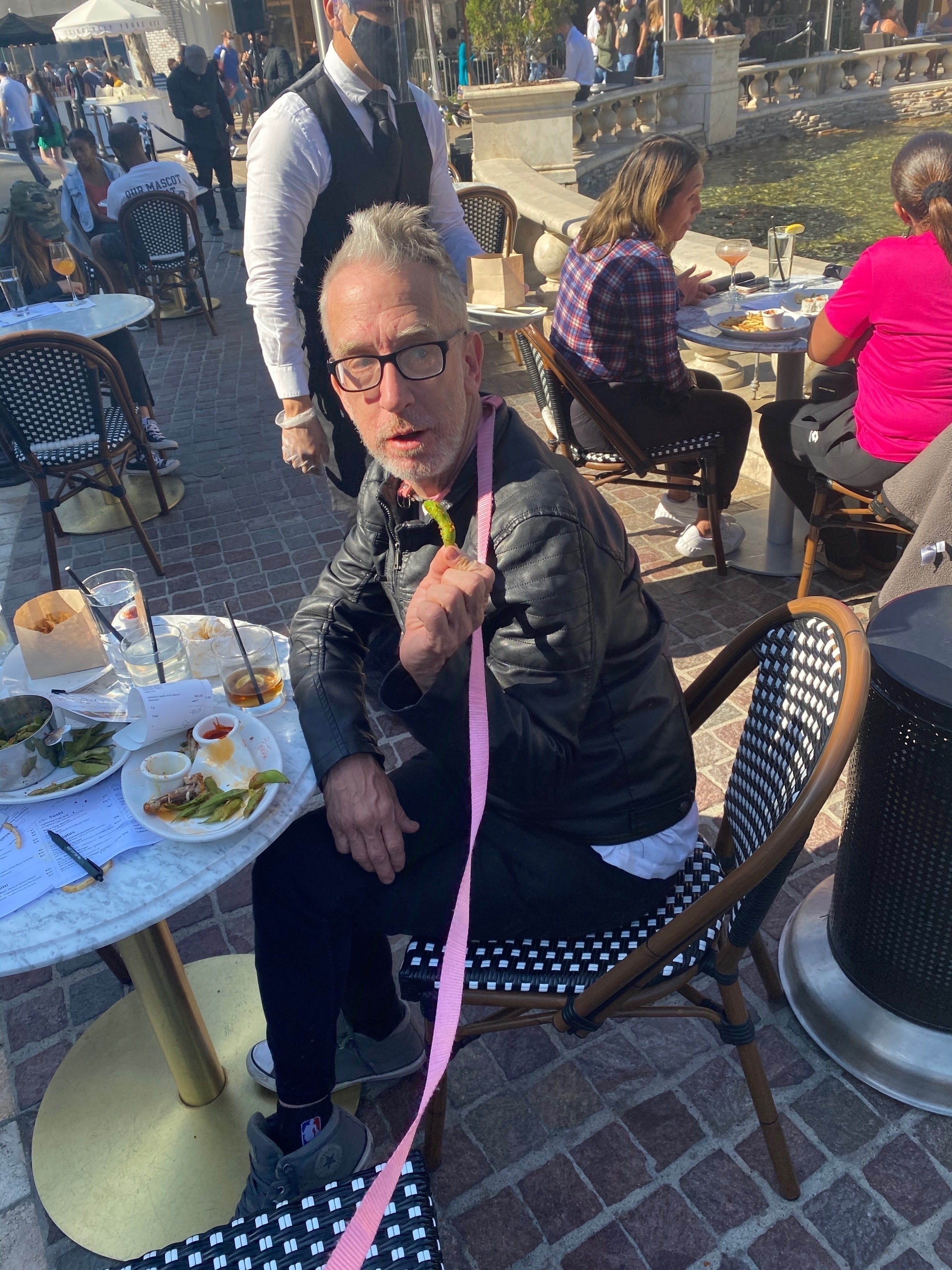 Andy Dick wearing a dog leash around his neck while eating outdoors.