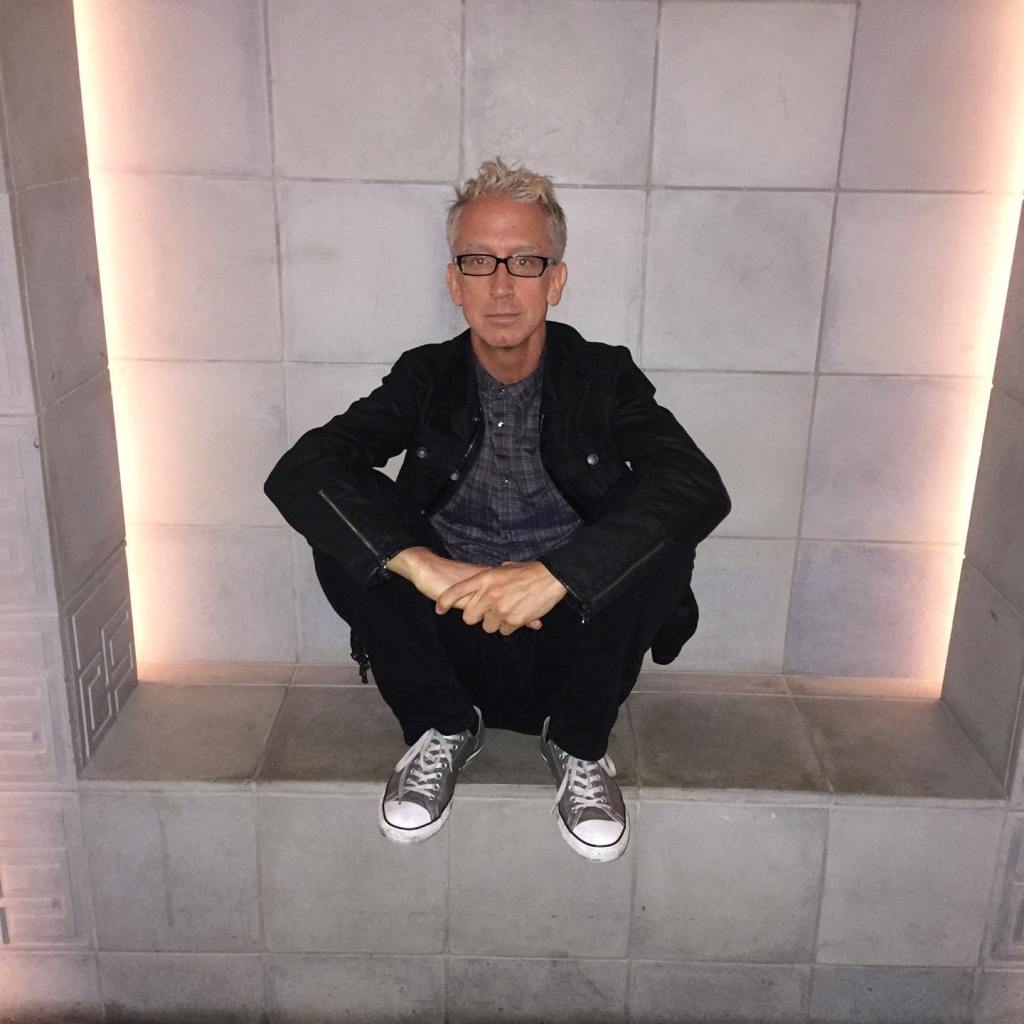 Andy Dick crouching on a ledge.