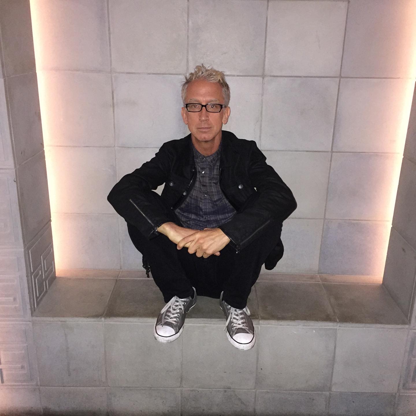 Andy Dick squatting with his hands clasped.