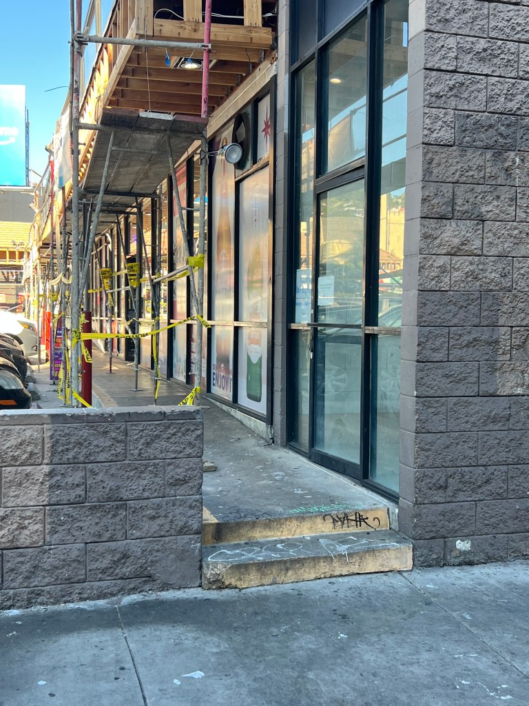 Sidewalk construction in front of a brick building with yellow caution tape.