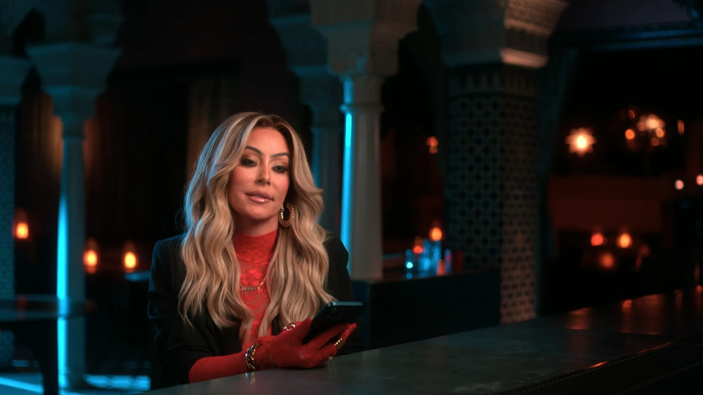 Aubrey O'Day sitting at a bar counter with a phone in her hands.